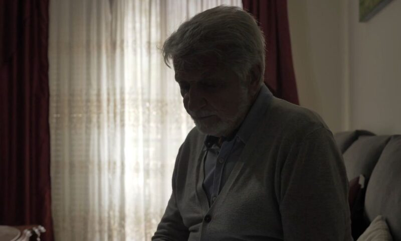 starac sedi u polu mračnoj prostoriji i gleda u pod